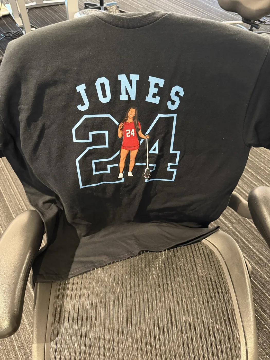 A black Jones 24 lacrosse tee laid over an office chair