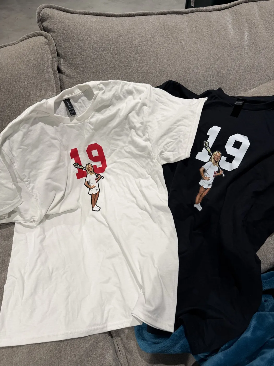 A white and a black number 19 lacrosse tee laid side by side on a couch