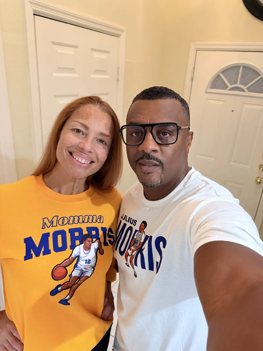 Two fans in Morris 12 tees, one gold and one white, smiling for a selfie