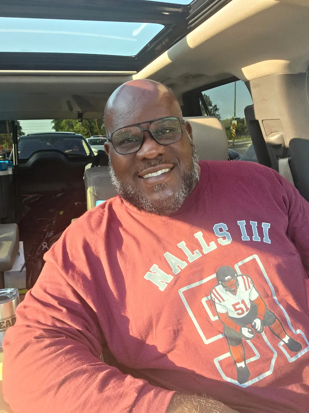 A fan in a maroon Nalls III 51 football sweatshirt smiling in a car