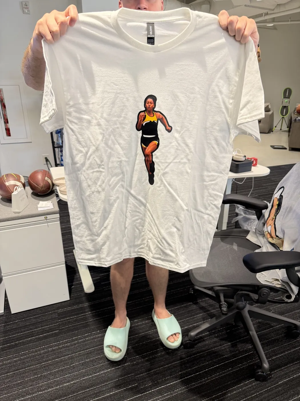 A white tee with a sprinter design held up in an office