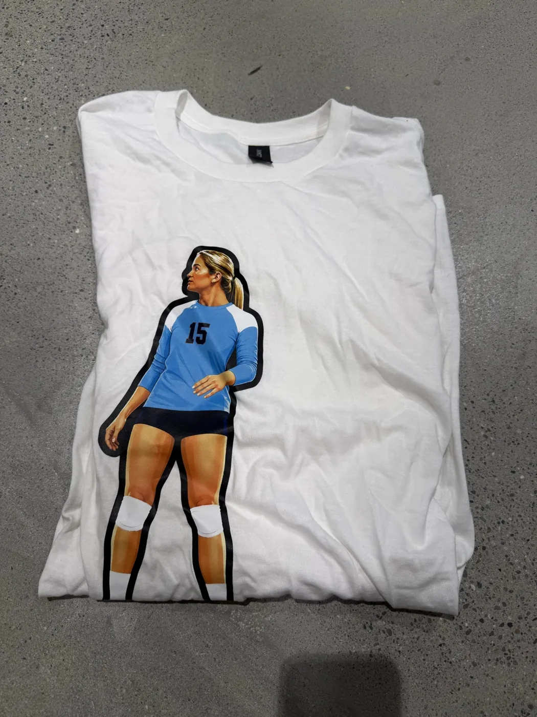A white tee with a number 15 volleyball player design, folded on a concrete floor